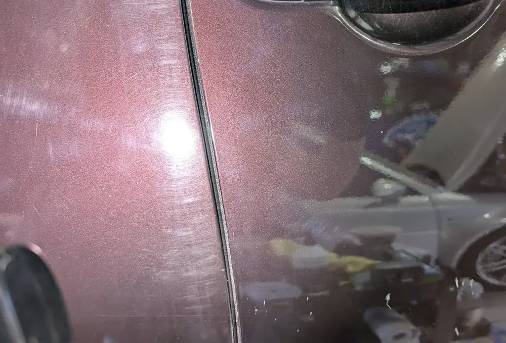 Close-up of maroon paint showing haze and surface marks under workshop lighting